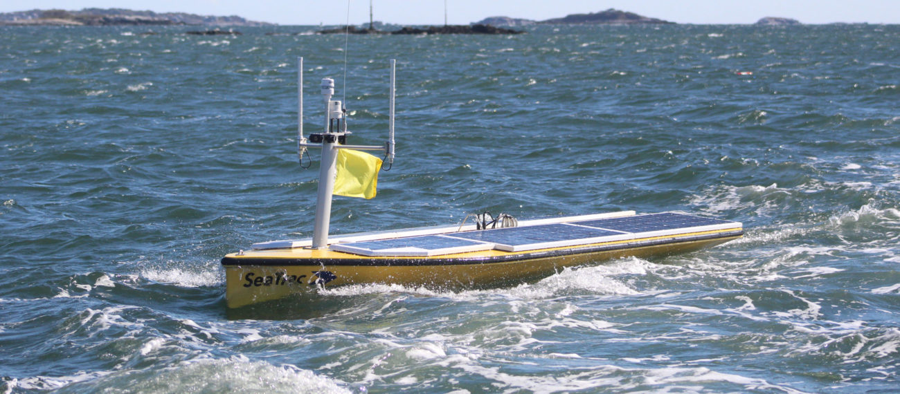 An unmanned surface vessel with solar cells, camera, GPS, weather monitoring sensors, and a capability of carrying a payload of 154 pounds is shown operating in a publicity photo.